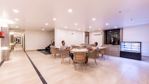 A modern hotel lobby with a reception desk, a display case, and a seating area with wicker chairs. - Hotel Maxx (Kohalpur)
