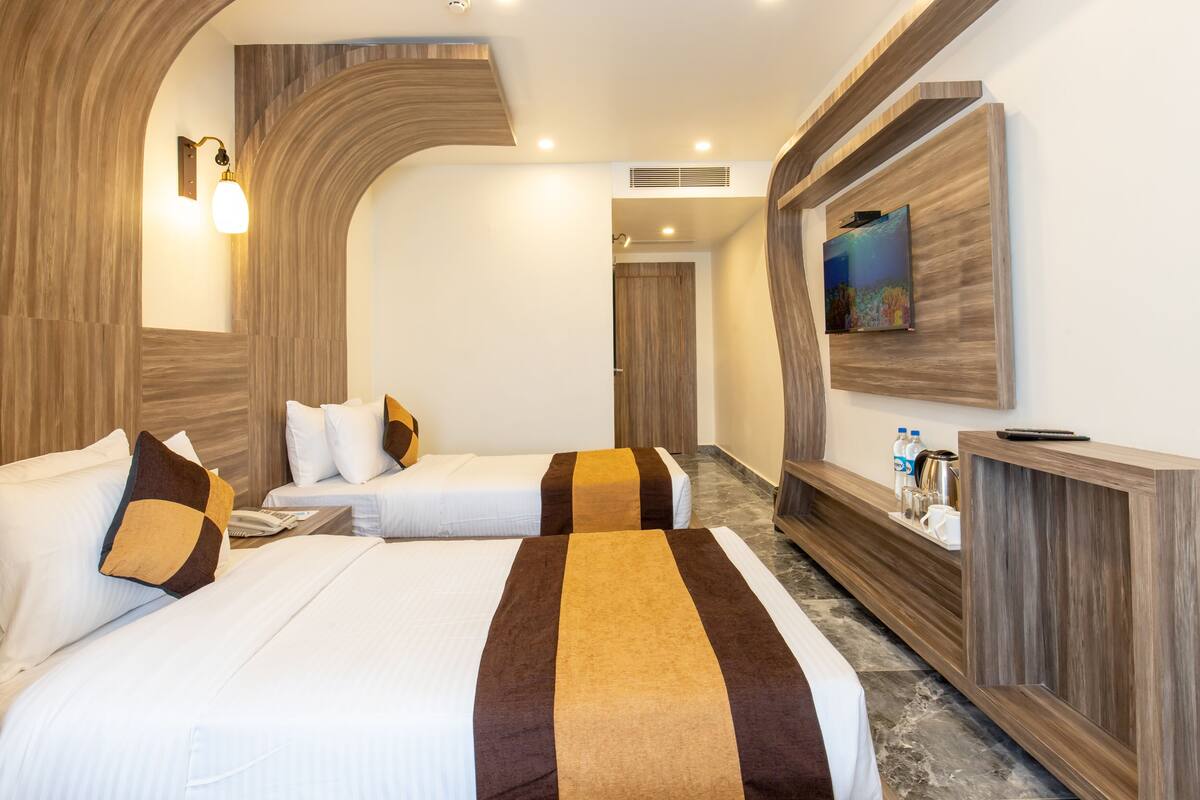 Une chambre d’hôtel avec deux lits, une tête de lit en bois, un grand tableau au mur et une table de chevet avec un téléphone et des bouteilles.