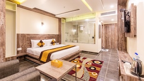 A hotel room with a large bed, a bedside table, a mirror, a shower area, and a TV mounted on the wall. - Hotel Maxx (Kohalpur)