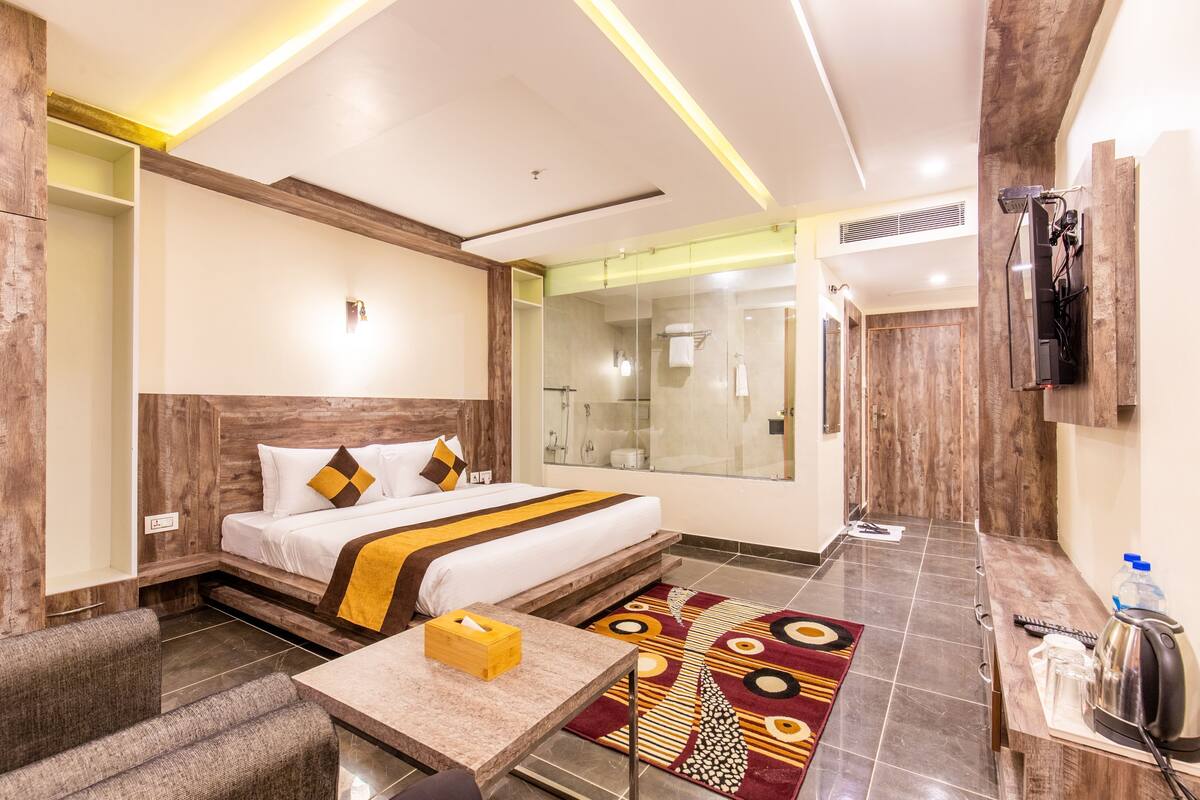 Une chambre d’hôtel comprenant un lit, une table avec une boîte de mouchoirs, un espace douche et un téléviseur fixé au mur.