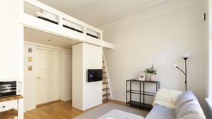 En moderne stue med en køjeseng, et fladskærms-tv, en sofa, et lille bord og en trappe.