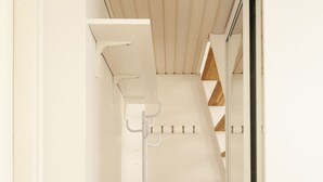 En smal gang med en hvid væg fra gulv til loft, en rund gulvlampe i hvidt og et lille sort bord med en hvid stol.