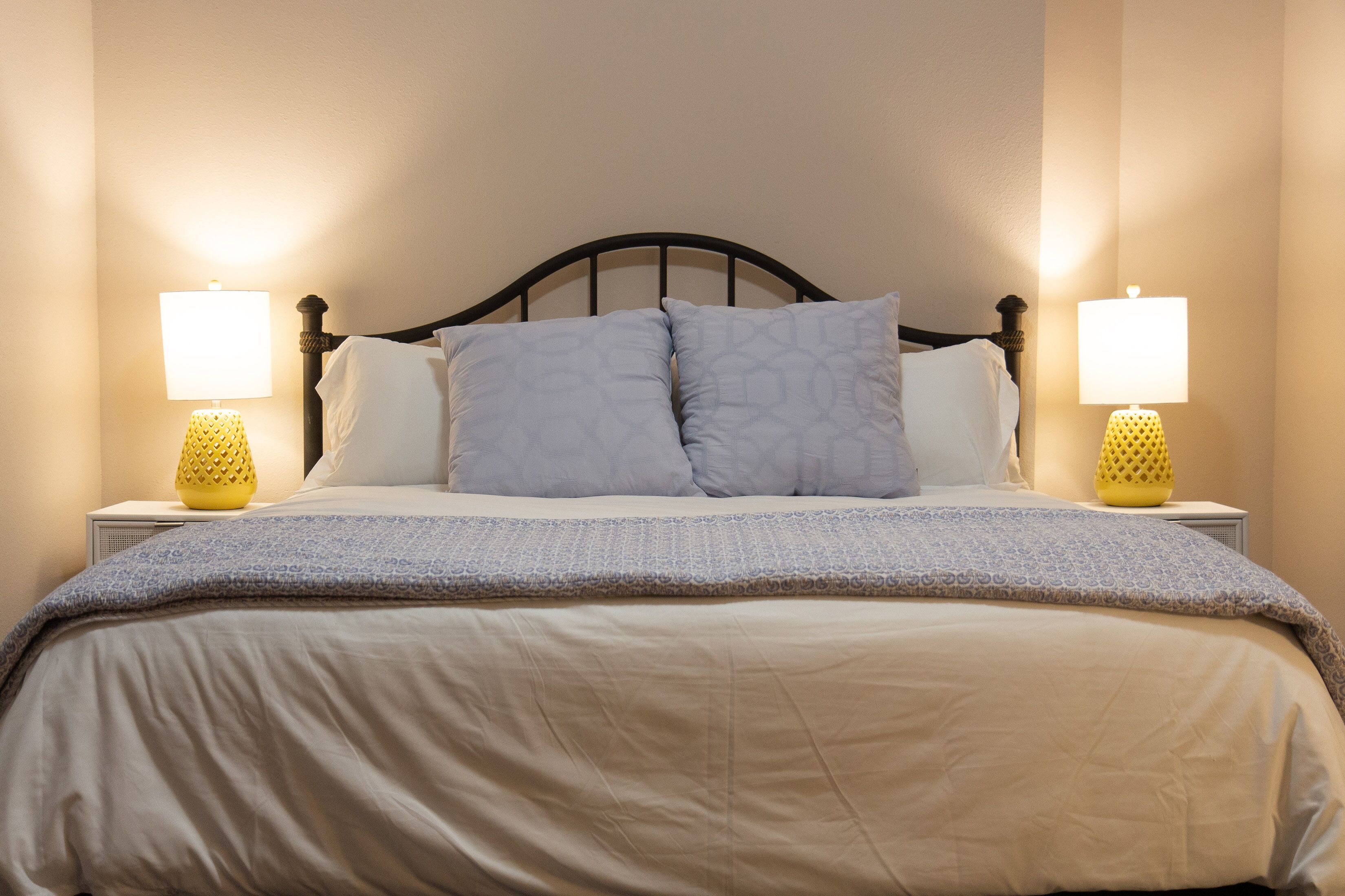 A neatly made bed with a headboard, two bedside lamps, and a patterned blanket.