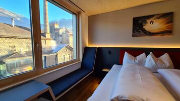 Une chambre d’hôtel avec une grande fenêtre, un lit, un banc et un tableau au mur.