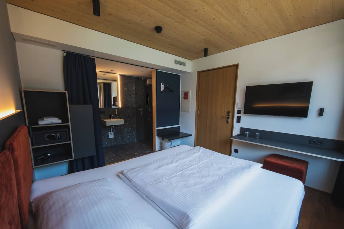 Habitación de hotel con cama, televisión, escritorio, espejo, armario y baño.