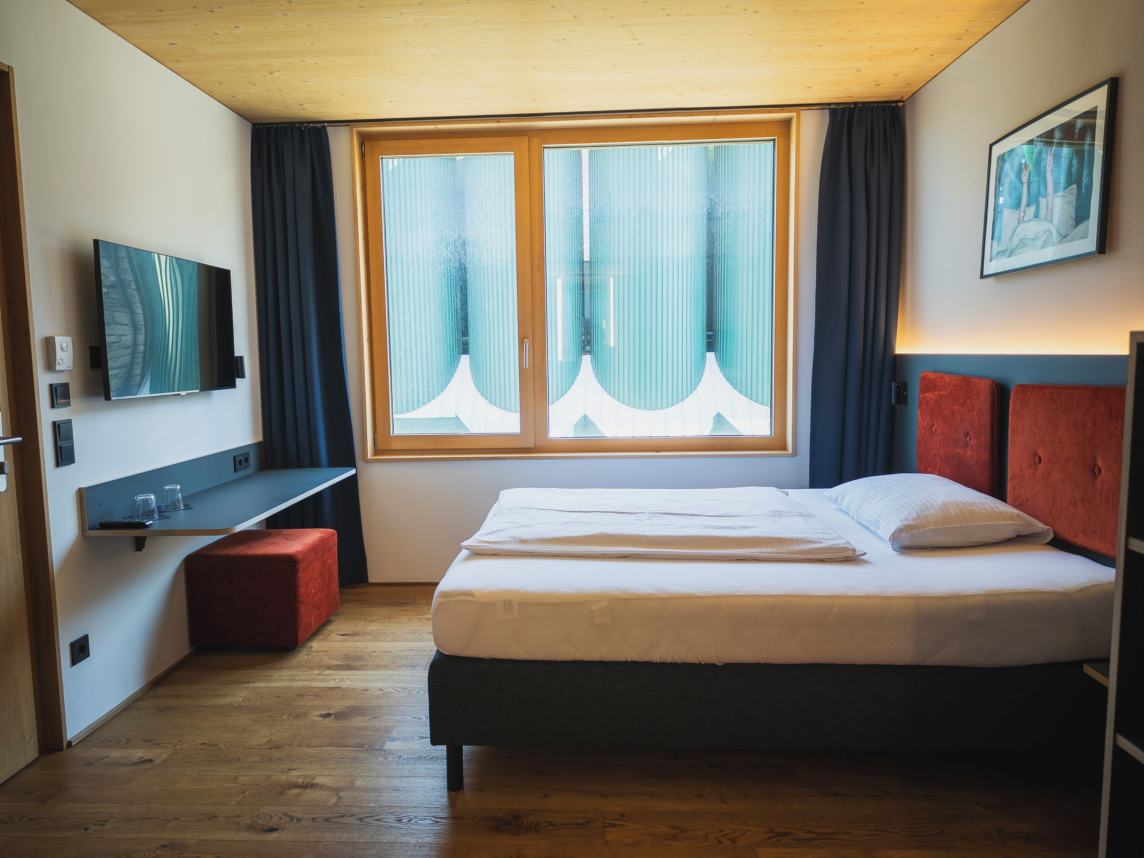 Une chambre d’hôtel avec un lit, une télévision, un bureau et une fenêtre avec des rideaux.