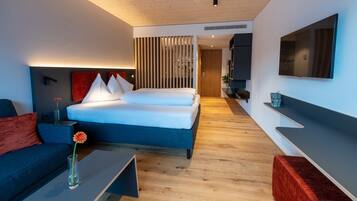 A modern hotel room with a large bed, a sofa, a coffee table with a vase, and a TV mounted on the wall.