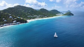 Une zone côtière avec un voilier, des collines verdoyantes et une plage.
