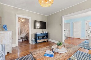 A living room with a wooden coffee table, a television mounted on the wall, a staircase leading to another room, and a door to the right.