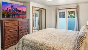 Ein Schlafzimmer mit einem großen Bett, einem Schminktisch, einem an der Wand befestigten Fernseher und Blick ins Freie durch ein Fenster.