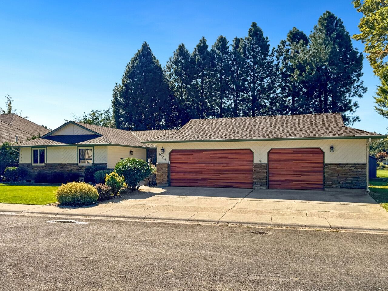 A single-story house with a garage, surrounded by a lawn and trees.