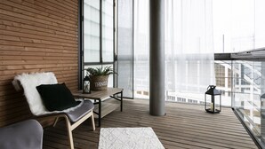 A balcony with wooden flooring, a white cushioned chair, a small table with a potted plant, and a lantern. - 1BR apartment with SPA in Kamppi Center (Helsinki)