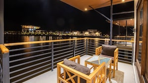 A balcony with a view of a river at night, featuring wooden furniture and a railing. - Lumbini Palace Resort (Dayanagar)