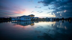 A waterfront property with a large building featuring multiple levels and a covered outdoor area. - Lumbini Palace Resort (Dayanagar)