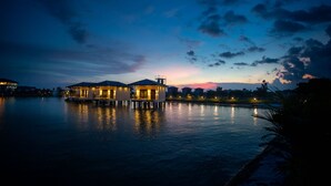 A waterfront property with multiple buildings, a dock, and a calm body of water reflecting the structures. - Lumbini Palace Resort (Dayanagar)