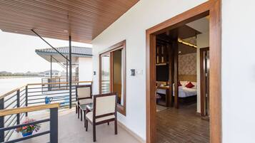 A balcony with wooden railings, a dining area with chairs, and a view of the water.