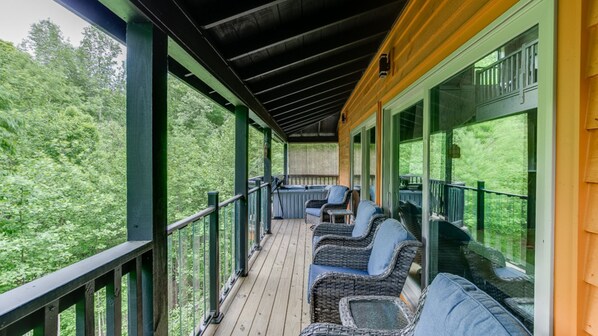 A covered deck with wicker furniture and glass doors overlooking a forested area.