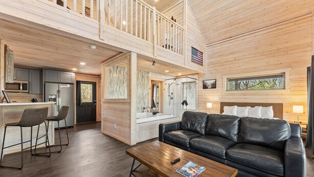 Een ruime woonruimte in loft-stijl met een hoge plafond, een houten balkon, een keuken met moderne apparatuur en een gezellige zithoek.