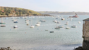 A harbor with numerous boats anchored in calm waters, a lighthouse in the distance, and a stone building on the right. - Sycamore Lodge (Helston)