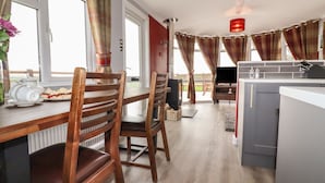 A cozy kitchen with wooden chairs, a dining table, a TV, and a red hanging light. - Sycamore Lodge (Helston)