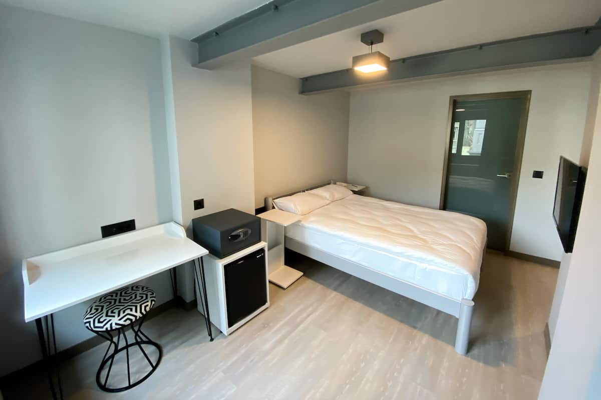A compact hotel room with a bed, bedside table, and a small desk with a chair.