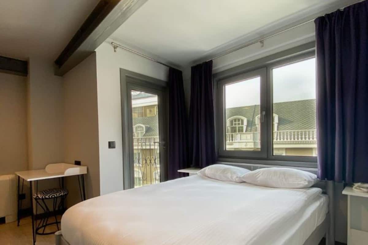 A bedroom with a large bed, a desk, and a window with curtains.