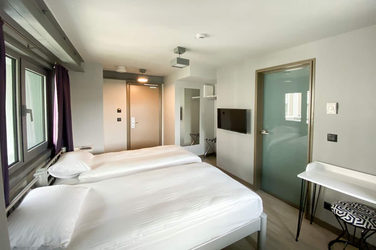 A hotel room with a bed, a desk, a TV, and a door.