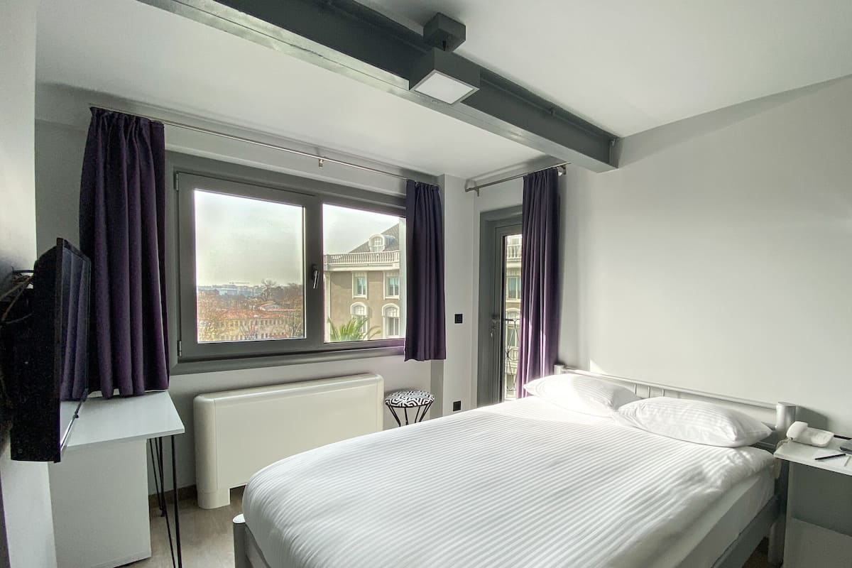 A modern bedroom with a large bed, a desk, and a window with curtains.