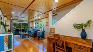A spacious living room with hardwood flooring, a wooden coffee table, a blue sofa, and a dining area with a wooden table and chairs. - Two homes w/ pool and hot tub near 3 beaches, Kihei (Kihei)