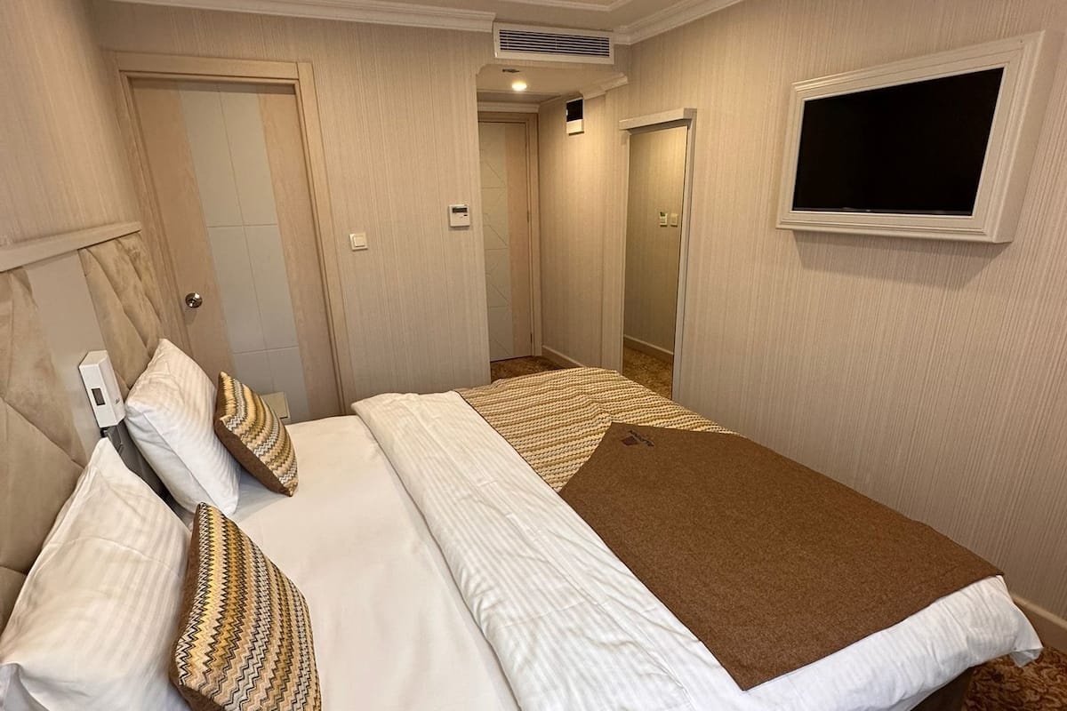 A hotel room with a bed, two pillows, a bedside table, a wall-mounted TV, and a door.