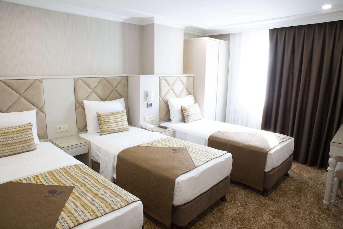 A hotel room with three single beds, each with a headboard, a bedside table, and a lamp.