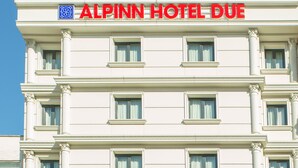 Fachada de hotel con el nombre "ALPINN HOTEL DUE" en letras rojas grandes.
