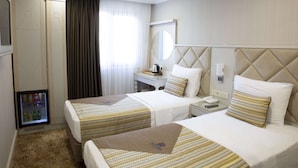 Habitación de hotel con dos camas, un minibar, un escritorio con teléfono y un espejo en la pared.