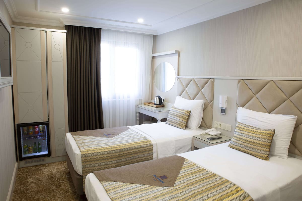 A hotel room with two beds, a minibar, a desk with a phone, and a mirror on the wall.