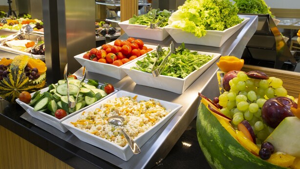 Un bufé con diversas opciones de comida, incluyendo ensaladas, frutas y platos de arroz.