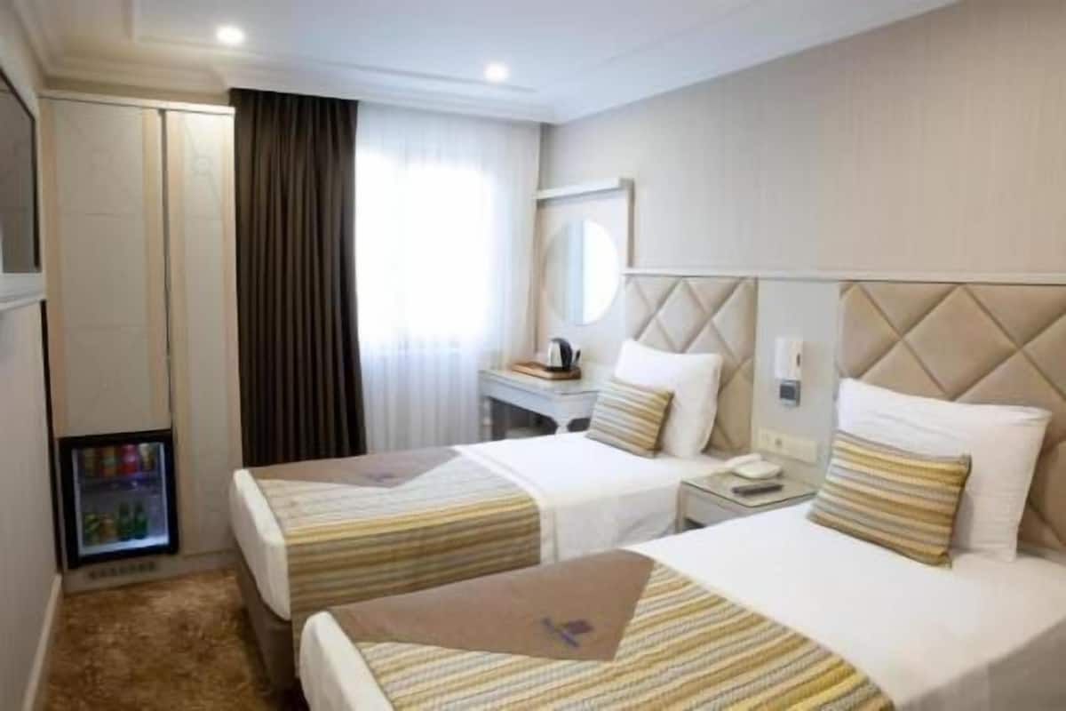 A hotel room with two beds, a minibar, a desk, and a mirror.