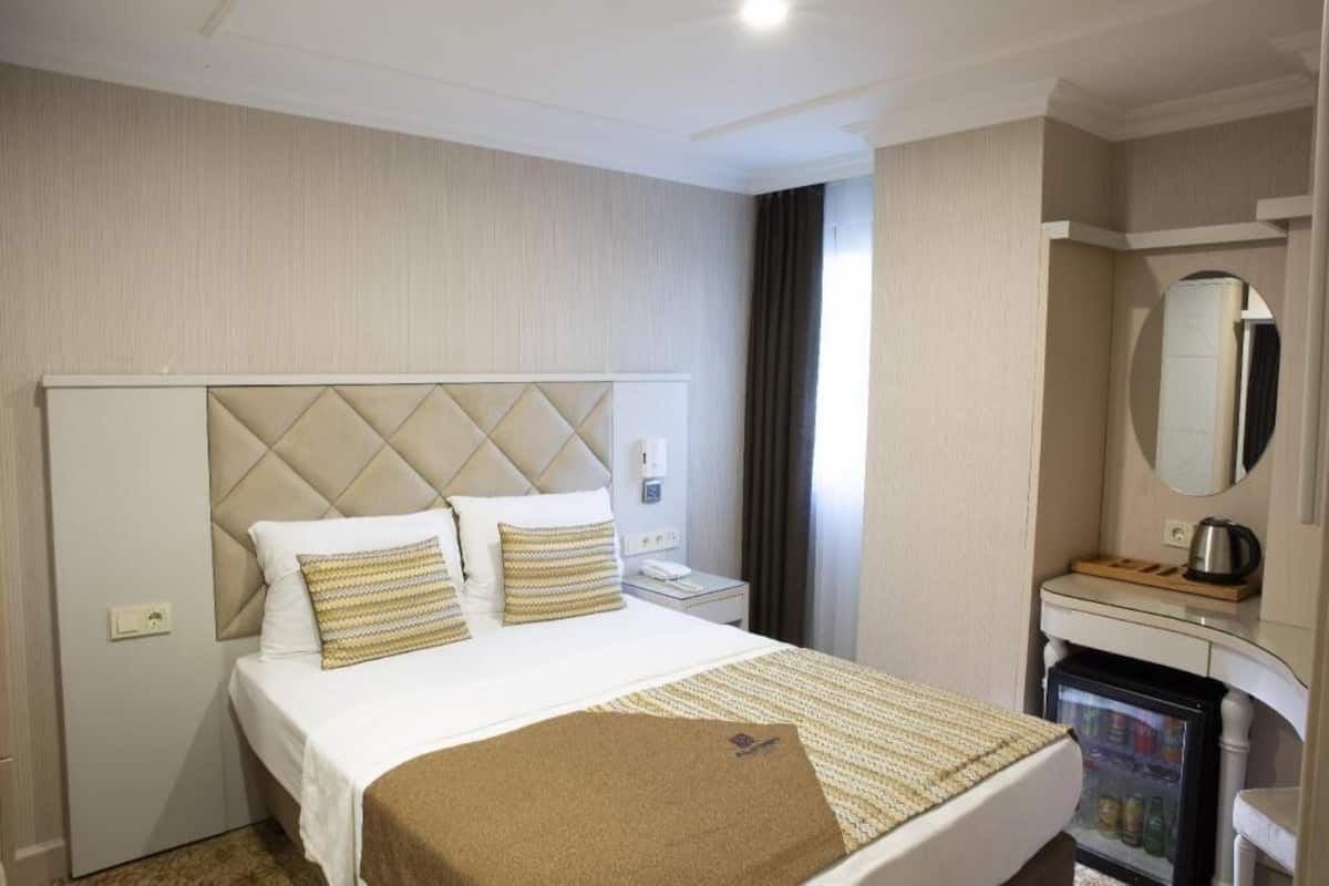 A hotel room with a bed, a nightstand, a minibar, and a mirror.