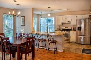 A modern kitchen with a central island, wooden dining table, and bar stools.