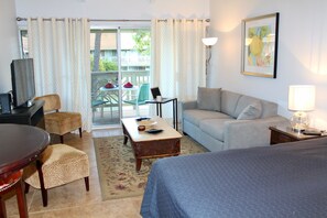 A hotel room with a bed, a sofa, a dining table with chairs, a TV, and a balcony with a table and chairs. - Kihei Bay Surf #218 Renovated, Near Beach, Shared Hot Tub, Inner Courtyard (Kihei)