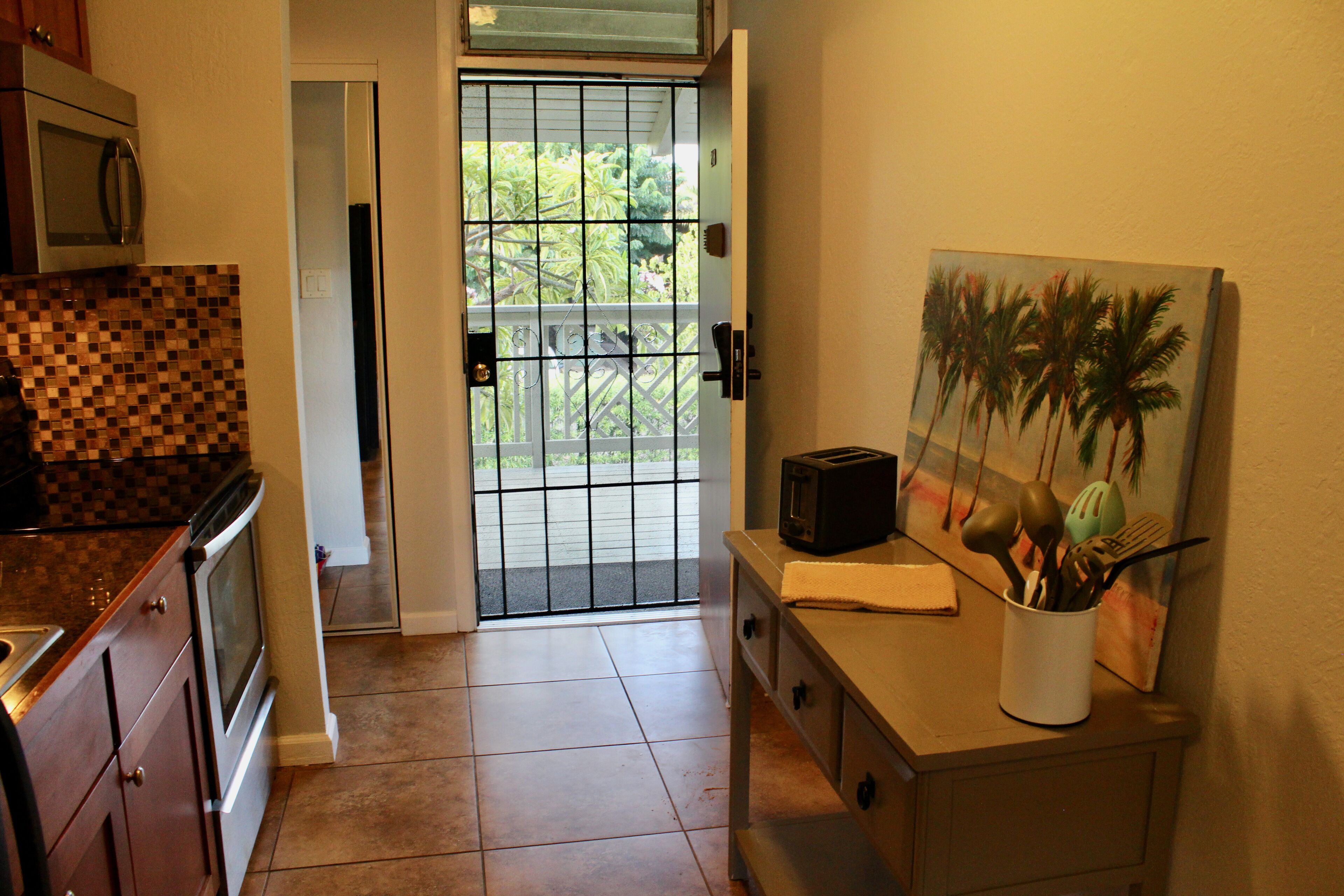 A kitchen with a microwave, oven, and a painting of palm trees.