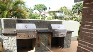 An outdoor barbecue area with two gas grills, stone countertops, and a stone wall backdrop.