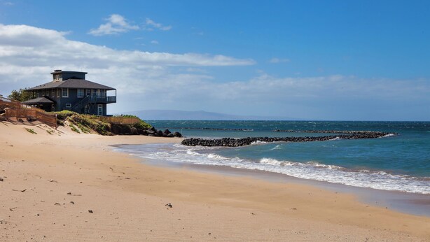 A beachfront property with a large house, a sandy beach, and a rocky breakwater.