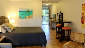 A bedroom with a bed, a desk, two chairs, and a painting of a beach scene.