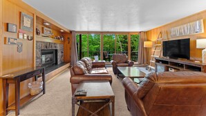 Un salón amplio con chimenea, sofás de cuero, televisor y un ventanal con vistas al exterior.