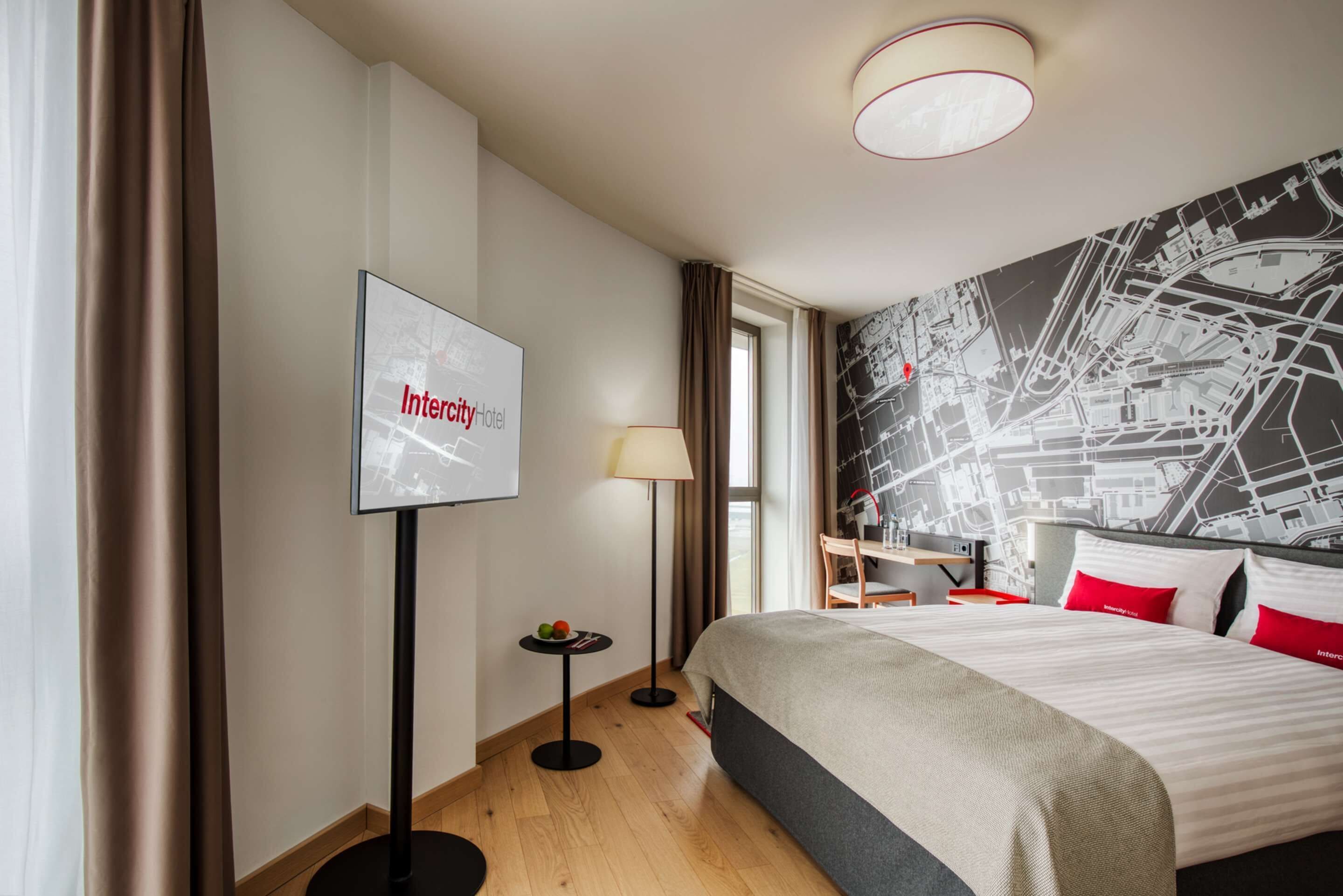 A hotel room with a bed, a map wall, a television, and a lamp.