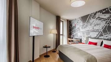 A hotel room with a bed, a map wall, a television, and a lamp.