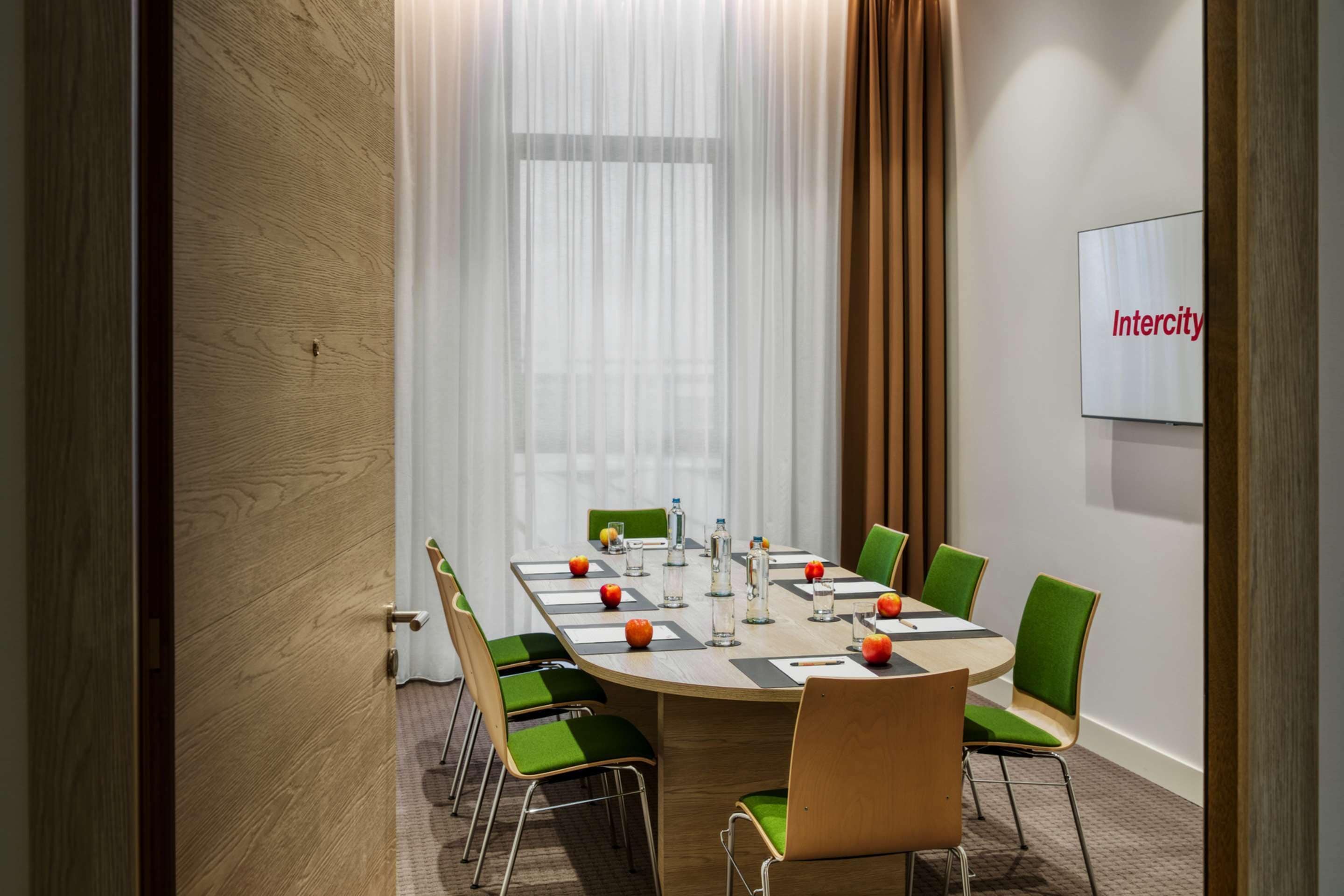Ein Konferenzraum mit rundem Tisch, grünen Stühlen und einer Tafel mit dem Schriftzug 'Intercity'.