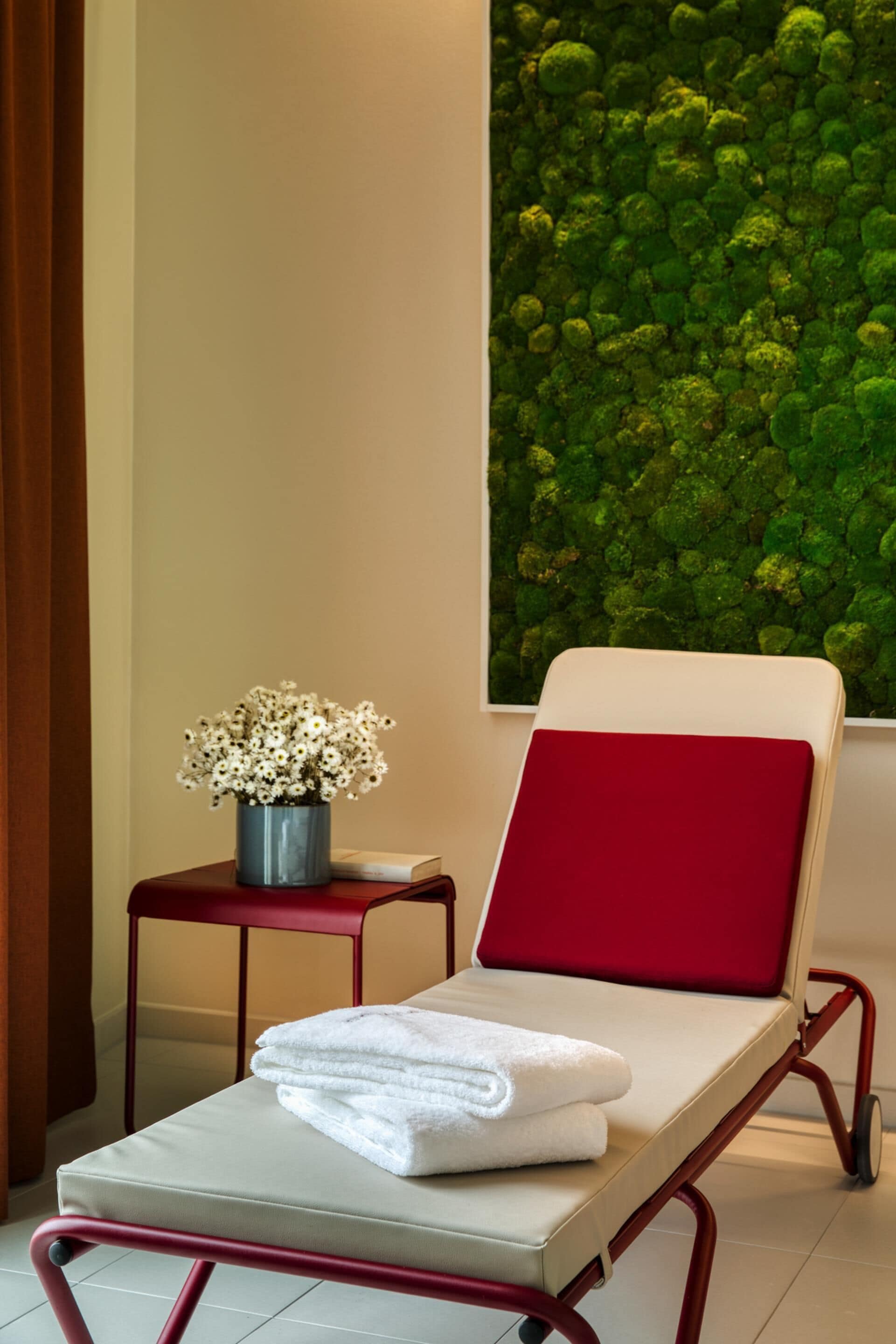 Una habitación con una butaca roja acolchada, una mesita con un florero y una pared cubierta de musgo verde.