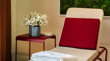 A room with a red cushioned chair, a small table with a flower vase, and a green moss wall.