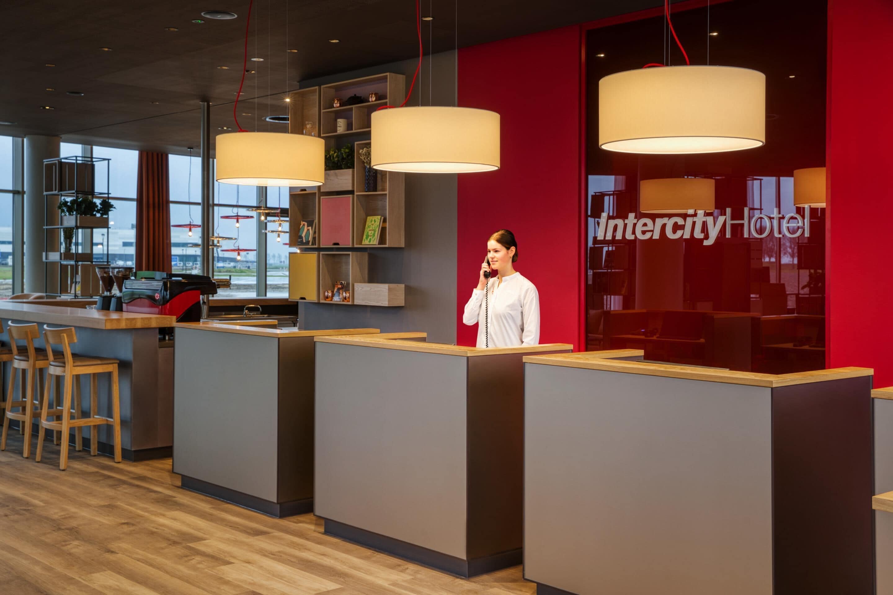 Een receptiegedeelte met een modern ontwerp, met een rode wand, een receptiebalie en een uitzicht op de skyline door grote ramen.